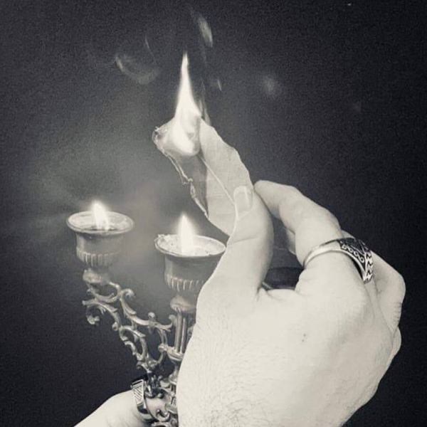 Candelabro retto da una mano con sopra di esso una foglia di salvia che brucia grazie alle fuoco delle candele, sorretta a sua volta dalla mano destra. Foto in bianco e nero.